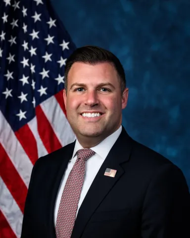 Smiling man in formal attire, flag backdrop
